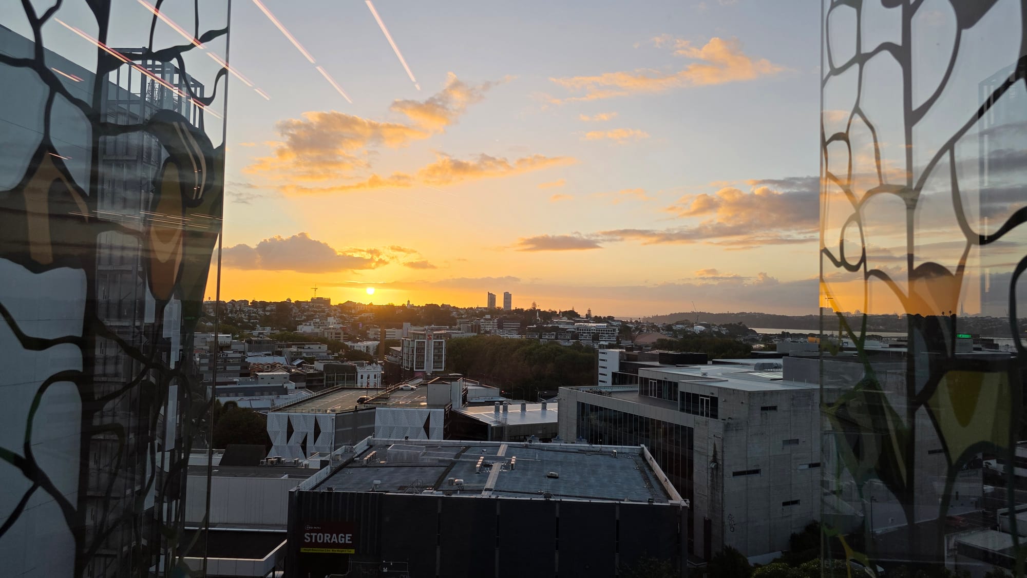Sunset over Freemans Bay, Ponsonby, Herne Bay from the NZICC venue Te Waha theatre lobby. Commercial buildings in shadow, a bright sun on near the horizon, orange fading to blue sky above